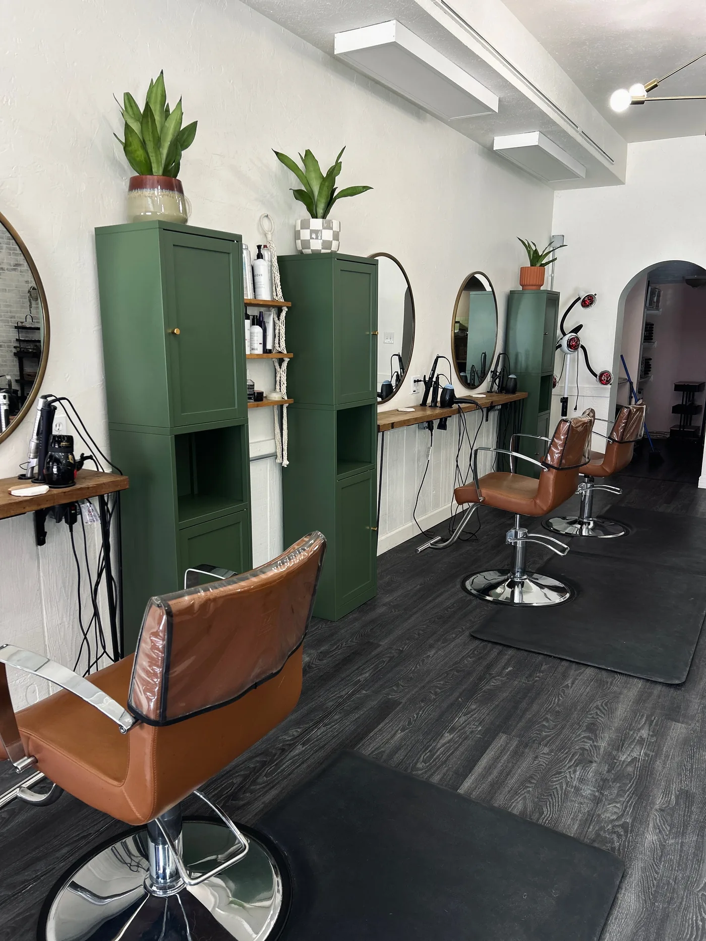 Inside Brushed On Main — styling stations with round mirrors, green cabinets, plants, and terracotta chairs